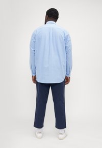 lichtblauw overhemd met lange mouwen, gecombineerd met een marineblauwe broek en witte schoenen. Heeft een afgeronde zoom en een losse pasvorm.