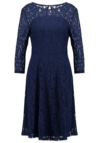 Marineblauwe kant jurk met een aansluitende top, driekwart mouwen en een uitlopende rok. Heeft bloemenpatronen en een sleufopening aan de achterkant.