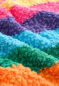 Colorful plush blanket featuring textured, fluffy fabric in stripes of pink, purple, blue, green, orange, and yellow.