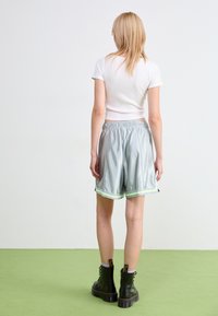 Light gray shorts with a shiny texture and an elastic waistband, featuring green accents at the hem. Paired with black waterproof boots.