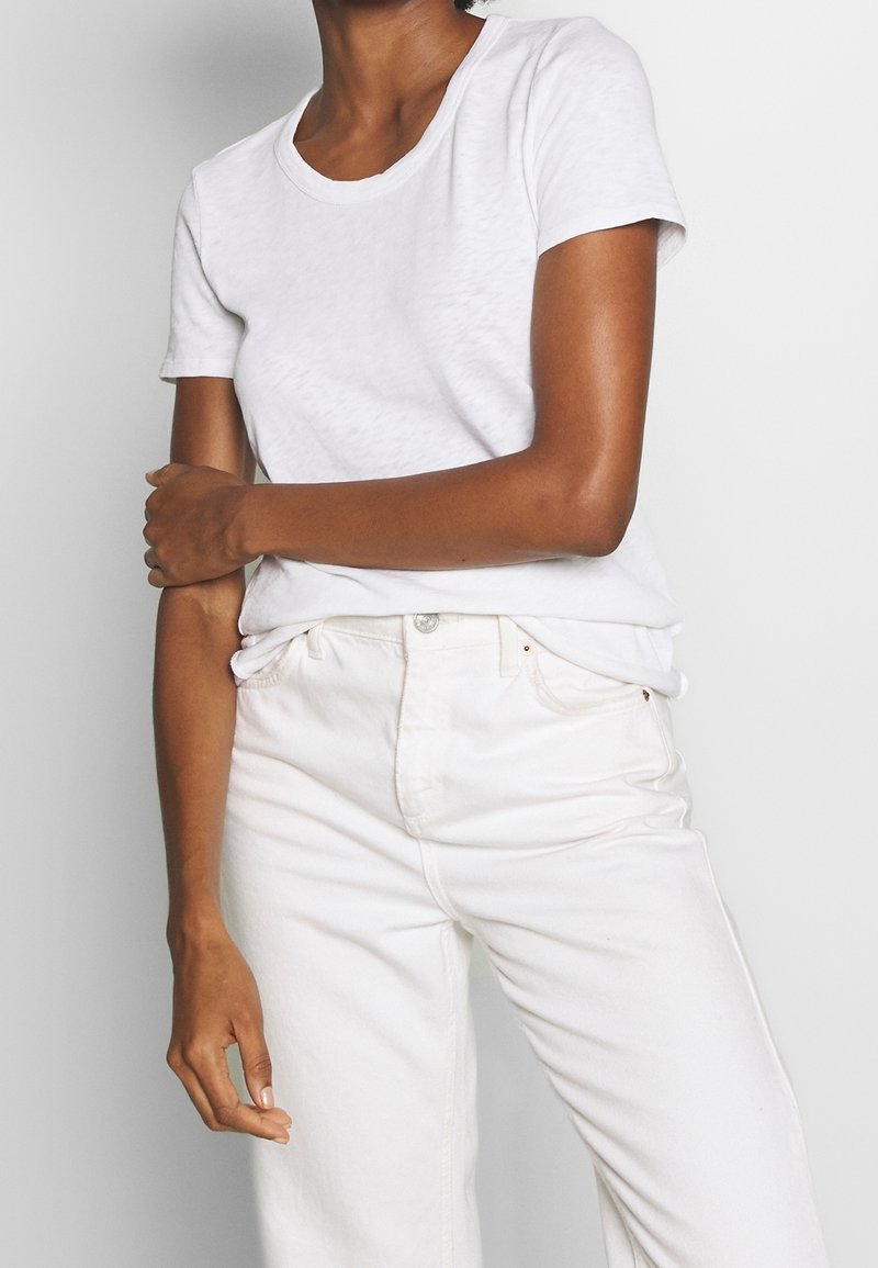 Camiseta blanca de manga corta con escote redondo, hecha de una tela suave. Combinada con unos jeans de mezclilla blancos de cintura alta.