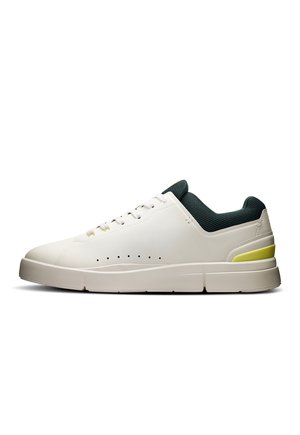 Sneaker bianco con colletto testurizzato verde, dettaglio giallo, design perforato sul lato, suola piatta e finitura liscia simile alla pelle.