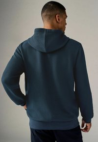 Sudadera con capucha en un tejido texturizado de color verde azulado oscuro, con un patrón de diamantes, mangas largas y un corte holgado. Cuerda ajustable en la capucha.