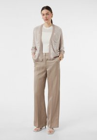 Jasno beżowy kardigan w kwiatowy wzór, zestawiony z szerokimi beżowymi spodniami i białymi sandałami na paski. Gładka tekstura, swobodny krój.