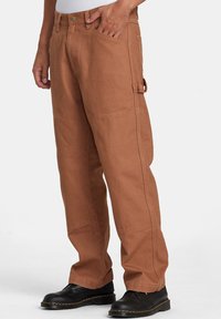 Brune cargo bukser lavet af kraftigt stof, med afslappet pasform, sidelomme og klassisk fem-lomme design. Båret med sorte støvler.