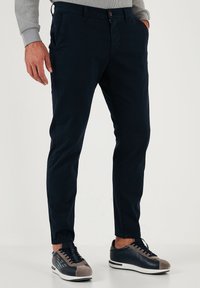 Navyblauwe broeken in een slim fit, gemaakt van een katoenmix. Voorzien van riemlussen, zijzakken en een knoopsluiting. Gepaard met grijze en navy sneakers.