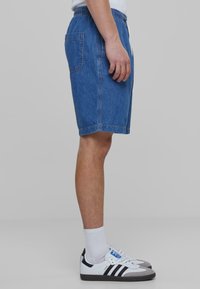 Džinsiniai šortai su elastine juosta, šoniniais kišenėmis ir vienu užpakaliniu kišeniu. Medžiaga yra mėlyna su kontrastingais siūlais, lygi tekstūra.