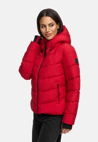 Červená puffa bunda so zipsom vpredu, s pripevnenou kapucňou a elastickými manžetami. Obsahuje prešívaný dizajn a kruhovú nášivku s logom na rukáve.