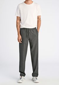 Grå vävda byxor med elastisk midja och dragband, i kombination med en åtsittande vit t-shirt och vita löparskor.