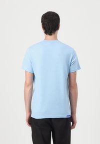 T-shirt à manches courtes bleu clair en coton, avec un col rond et une petite étiquette logo en bas à gauche.