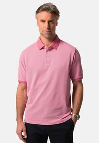 Rosa pikétröja i strukturerad tyg, med krage, tre knappar och korta ärmar. Bärs med mörka byxor.