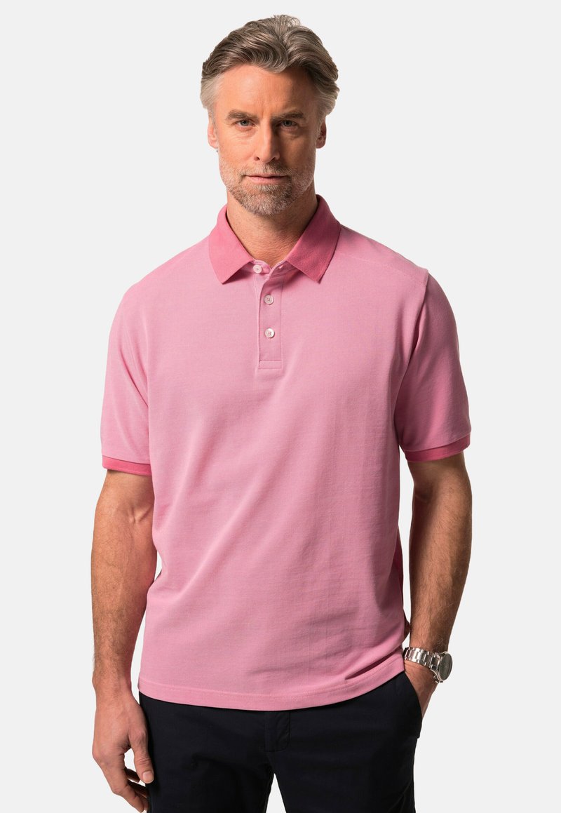 Rosa pikétröja i strukturerad tyg, med krage, tre knappar och korta ärmar. Bärs med mörka byxor.