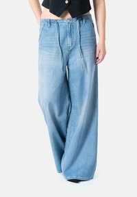 Wide-leg blue denim jeans with a loose fit, drawstring closure, and a light wash, featuring front pockets and a slightly faded texture.