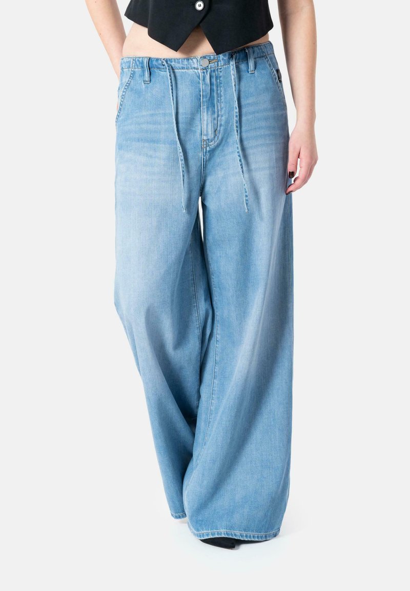 Wide-leg blue denim jeans with a loose fit, drawstring closure, and a light wash, featuring front pockets and a slightly faded texture.