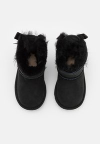 Bottines noires en daim souple avec une doublure en fausse fourrure, présentant une couture et deux languettes en tissu à l'arrière.