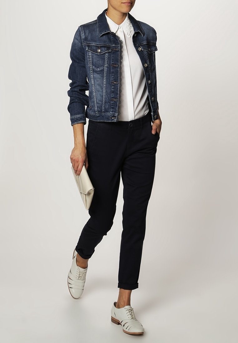 Jeansowa kurtka, biała bluzka z kołnierzykiem, ciemne spodnie i jasne buty. W ręku torebka kopertówka. Kurtka ma kieszenie i zapięcie na guziki.