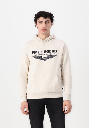 Cream hoodie with front pocket, drawstring hood, and navy graphic text "PME LEGEND American Classic" with wing design. Cotton blend fabric.