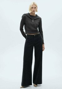 Grå zip-tröja med ribbad textur, kombinerad med högmidjade, vida svarta jeans med en subtil mönstring och knappflik framtill.