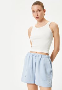 Camiseta de tirantes blanca de canalé y pantalones cortos azul claro con cinturilla elástica, que cuentan con dos bolsillos laterales y un corte relajado. Textura suave.