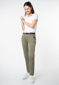 Khaki katoenbroek met een rechte pasvorm, voorzien van zijzakken, een zwarte geweven riem en witte sneakers. Vergezeld van een plain wit t-shirt.