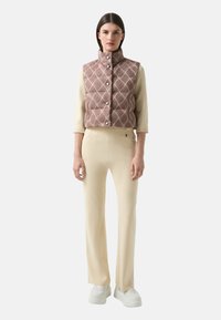 Padded vest w kolorze burgundowym z białym wzorem fal, z wysokim kołnierzem i guzikami, w połączeniu z dopasowanymi spodniami w kolorze kremowym i białymi butami.