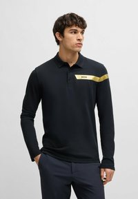 Langärmliges schwarzes Polohemd mit spitzem Kragen, das einen goldenen und weißen Logostreifen über der Brust aufweist, aus glattem Stoff gefertigt.