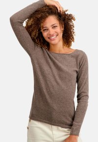 Pull marron à manches longues en texture douce avec un col bateau, présentant une coupe décontractée et un ourlet droit, porté avec un pantalon crème.