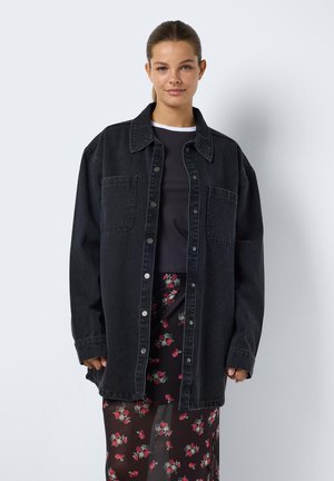Tumman denim-tyyppinen yöpaita, jossa on napit, kaksi etutaskua ja rento leikkaus. Päällä musta toppi ja läpinäkyvä kukkamekko.