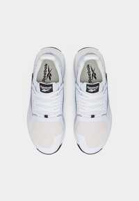 Ζευγάρι λευκά παπούτσια τρεξίματος Reebok με πλέγμα στις μύτες και μαύρο λογότυπο Reebok στη γλώσσα και στις εσωτερικές σόλες, εμφανιζόμενα από πάνω.