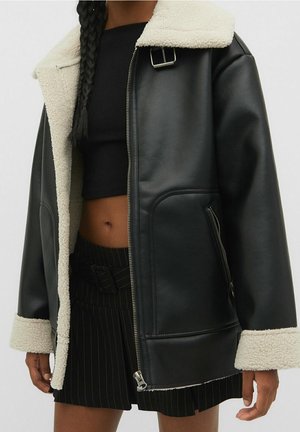 Woman wearing black faux leather jacket with white fleece lining, black crop top, and black pinstripe skirt, showing midriff and braids.