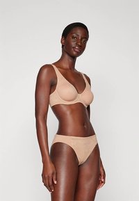 Set di reggiseno e slip coordinato beige, realizzato in un morbido tessuto, caratterizzato da un design minimalista con bordi lisci e senza hardware visibile.