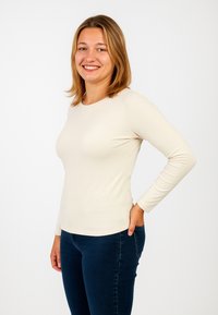 Maglietta beige a maniche lunghe realizzata in tessuto morbido, con scollo rotondo e vestibilità slim, abbinata a jeans aderenti di colore blu scuro.