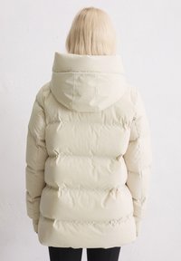Beige pufferjack met een capuchon, met geblokte secties en een gladde textuur. Het ontwerp is lichtgewicht en biedt isolatie.