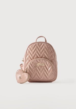Sac à dos matelassé rose clair avec poche zippée à l'avant, logo doré "Guess" et porte-monnaie en forme de cœur fixé sur fond blanc.