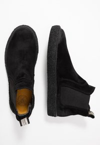 Stivali alla caviglia in suede nero con pannelli laterali elasticizzati e suole in gomma texture, dotati di un occhiello sul retro per un facile indossamento.