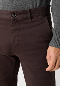 Dark brown trousers made of soft fabric, featuring a button closure and side pockets. The waistband has a drawstring for adjustable fit.