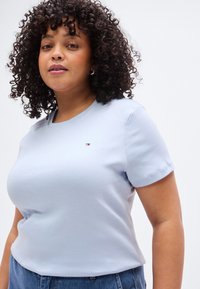 Ανοιχτό μπλε βαμβακερό κοντομάνικο t-shirt με στρογγυλή λαιμόκοψη και μικρή λεπτομέρεια λογότυπου στο στήθος, φορεμένο από ένα άτομο με σγουρά μαλλιά.