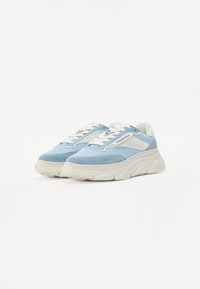 Lyseblå sneakers med teksturert semsket overdel, hvite detaljer, tykk gummisåle og flate snøringer. Har et mesh-panel for pusteevne.