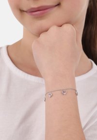 Bracciale in argento con quattro piccoli charm a forma di cuore con accenti rosa, indossato su un polso su uno sfondo chiaro.