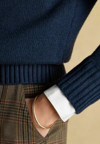 Tumedate kootud sviiter ribaga äärisega, koos ruuduliste pükste ja valge särgiga. Kuldne käevõru lebab randmel.