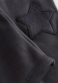 Tela de algodón gris oscuro con un parche de estrella negra de fieltro con bordes bordados. Textura suave con detalles de costuras visibles.