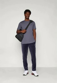 T-shirt cinza de mangas curtas, calças de veludo azul-escuras e ténis brancos. Mala de ombro preta. Design simples, ajuste descontraído.