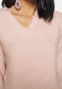 Light pink, ribbed knit sweater featuring a V-neck design and loose fit. Soft texture with visible stitching details.