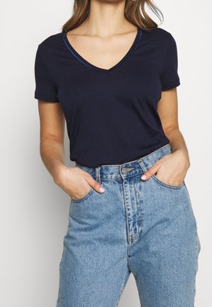 Granatowy t-shirt z dekoltem w serek i krótkimi rękawami, wykonany z miękkiego materiału. Połączony z jasnoniebieskimi, wysokim stanem dżinsami z przodu zapinanymi na guziki.