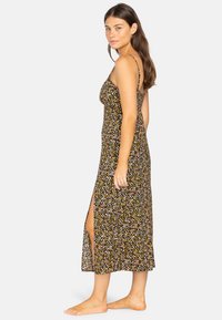 Abito maxi floreale con spalline sottili, base nera e modelli di fiori multicolori. Presenta uno spacco laterale e un tessuto leggero.
