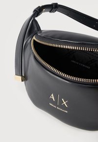 Μαύρο δερμάτινο τσαντάκι Armani Exchange με χρυστό φερμουάρ, ρυθμιζόμενο λουρί και χρυσλό λογότυπο στο μπροστινό μέρος, μερικώς ανοιχτό για να φαίνεται η εσωτερική επένδυση.