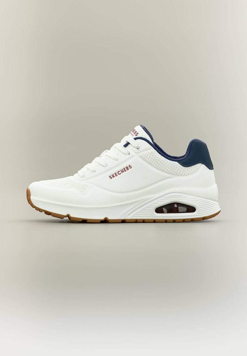 Λευκό αθλητικό παπούτσι Skechers με ναυτικό γιακά, ορατό αερόσακο στη σόλα και καουτσούκ σόλα χρώματος καφέ σε απλό γκρι φόντο.