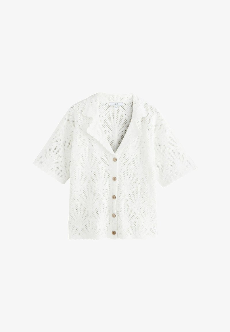 Cardigan blanc à manches courtes en dentelle avec bords festonnés, motif floral, boutons marron et col pointu.