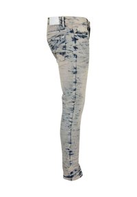 Uske traperice u svijetlom bež denimu s plavim tie-dye uzorkom. Ima pet džepova, petlje za remen i bijelu oznaku na rubu struka.
