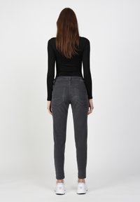 Graue Slim-Fit-Hosen aus weichem Material, mit leicht glänzenden Gesäßtaschen. Kombiniert mit weißen Sportschuhen, von hinten betrachtet.